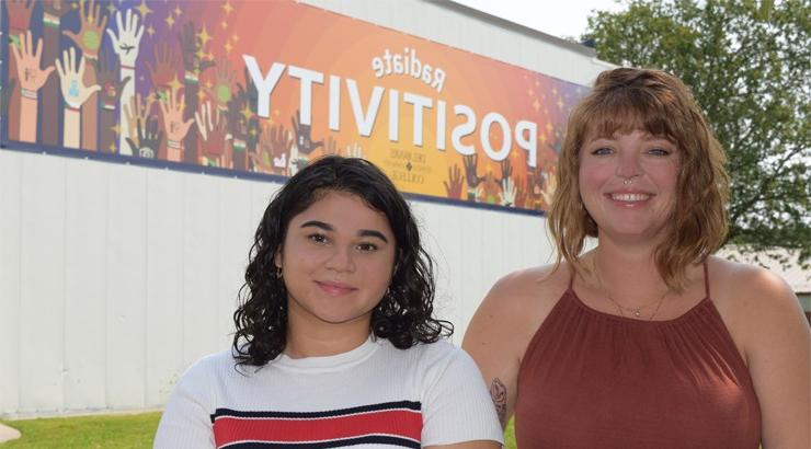 Amanda Baez and Amanda Sudowsky in front of a large banner with the words 